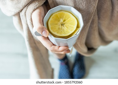 A Young White Woman Covered In A Cozy Blanket Holds A Mug Of Tea With A Lemon Slice In Her Hands