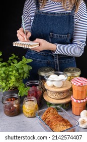 Young white woman dressed in denim apron in the right part writing the weekly list of prepared homemade food. Elegant batch cooking scene. - Shutterstock ID 2142574407