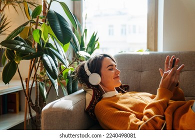 Young white woman in headphones using cellphone while lying on couch at home - Powered by Shutterstock