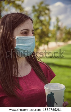Young white woman holds a recyclable cup while enjoying a nice day in the park during coronavirus period.