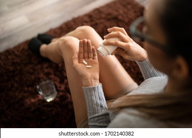 Young White Woman At Home Holding Two Pain Killer Pills In Her Hand Palm After Spilling From Bottle And Glass Of Water. Concept Of Pain Relief, Addiction To Opioids And NSAIDs