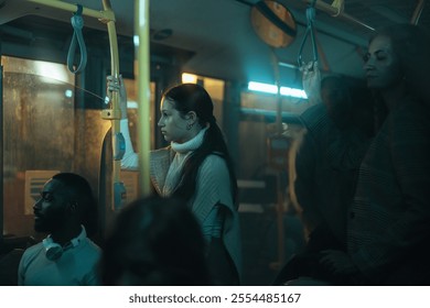 Young white woman with long brown hair standing on a crowded bus at night holding onto a handrail. - Powered by Shutterstock