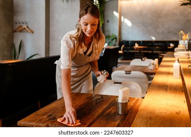 Young white woman wearing apron cleaning table while working in restaurant - Powered by Shutterstock