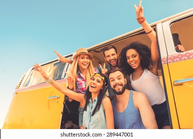 Young wild and free. Low angle view of group of young happy people having fun together while sitting inside of retro mini van 