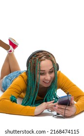 Young Winsome Positive Caucasian Female with African American Dreadlocks Listens Music in Wirreless Headphones Smartphone While Laying on Floor Over White. Vertical Shot