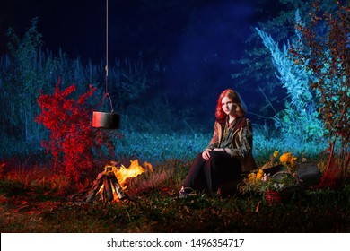 young witch by  fire in night forest prepares  magic potion