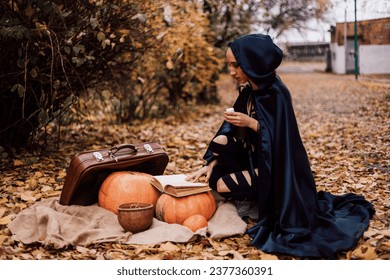 A young witch in the forest makes a spell, reads a book. Magic in the forest. Halloween. High quality photo