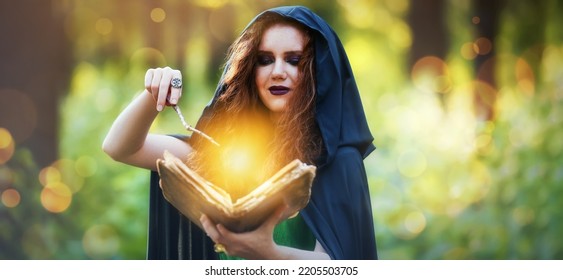 Young Witch With Spell Book And Magic Wand In Green Forest