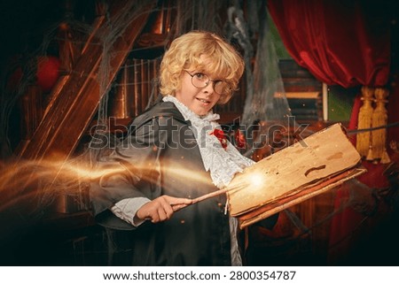 Young wizard casting a magical spell with wand and ancient book in a mysterious library. Halloween fantasy concept with glowing light, magic and imagination.