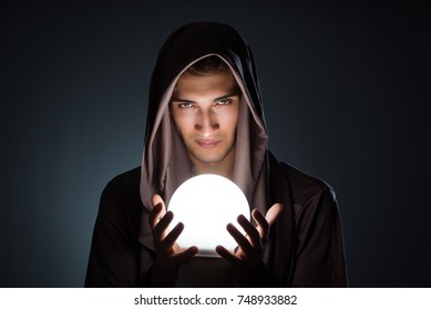 Young wizard with crystal ball in dark room