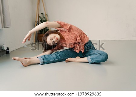 Young woma enjoying a relaxing yoga workout on the floor at home doing a graceful side stretch with eyes closed and a smile of pleasure in a health and fitness concept