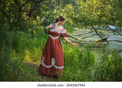A young woman in a 19th century dress by the river. Girl with a book in his hand, summer day.