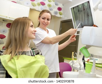 Young Woman 20-25 Years Old On A Review Of Woman Dentist, Sitting In Armchair In Dental Clinic. Dentist Female Explaining X-Ray To Patient. Dentistry, Medicine And Health Care Concept