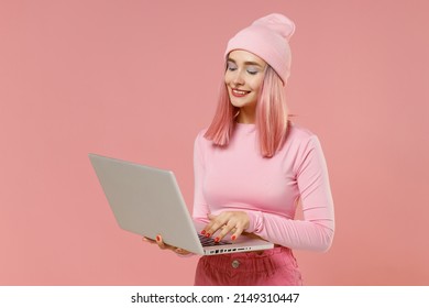 Young Woman 20s With Bright Dyed Rose Hair In Rosy Top Shirt Hat Hold Use Work On Laptop Pc Computer Isolated On Plain Light Pastel Pink Background Studio Portrait. People Lifestyle Fashion Concept