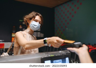 Young Woman 20s In Casual Clothes Mask Shopping At Supermaket With Grocery Cart Put Credit Card To Modern Bank Payment Terminal To Process Acquire Payments At Checkout Near Cashier Inside Store Cafe