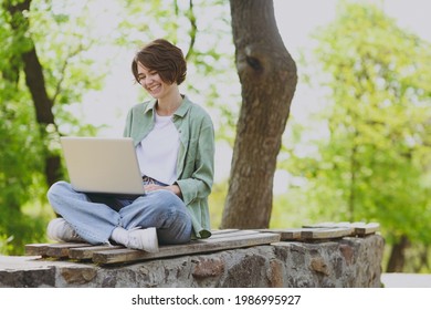 Young woman 20s wears mint shirt white t-shirt user work on laptop pc computer sit on bench rest relax in spring green city park sunshine outdoors on nature. Mobile office freelance business concept