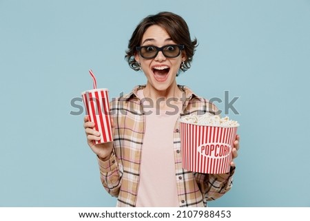 Young woman in 3d glasses watch movie film hold bucket of popcorn cup of soda cola water isolated on pastel plain light blue background studio portrait. People emotions in cinema lifestyle concept.