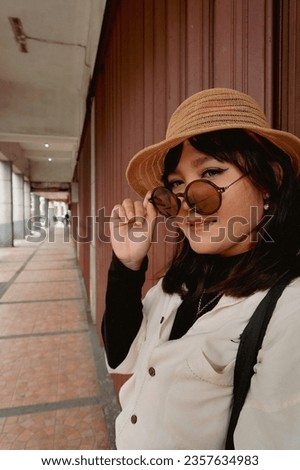 Young woman in 90s casual look photo concept wearing summer hat, sunglasses and tote bag. Vacation style for walk around in town. 