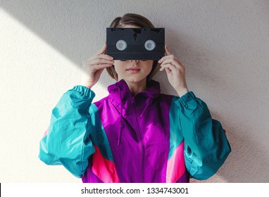 Young Woman In 90s Style Clothes Holding VHS Cassette On White Background