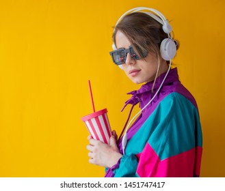 Young Woman In 90s Style Clothes With Cup And Headphones On Yellow Background