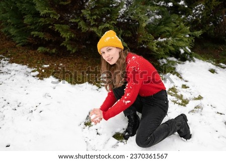 A young woman is about to throw a snowball while in the snow on the background of Christmas trees outdoors. Concept of winter fun and activities, New Year celebration