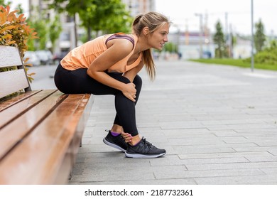 Young Woman With Aching Leg. Sportswoman With Injured Ankle. Runner Girl Is Holding Her Injured Leg. Athlete Woman Has Ankle Injury, Sprained Ankle During Running Training