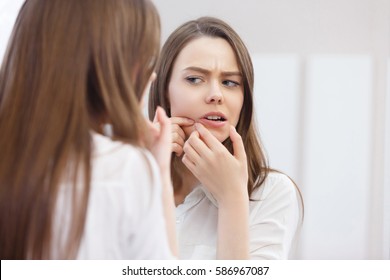Young woman with acne. Portrait of teenager Girl looking at the mirror. Beauty, skin care lifestyle concept.