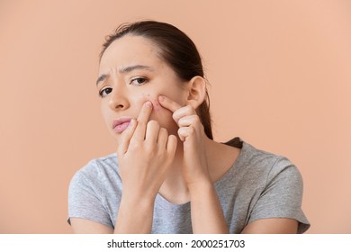 Young Woman With Acne Problem Squishing Pimples On Color Background