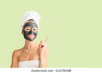 Young woman with activated charcoal mask on her face pointing at something on color background - Powered by Shutterstock