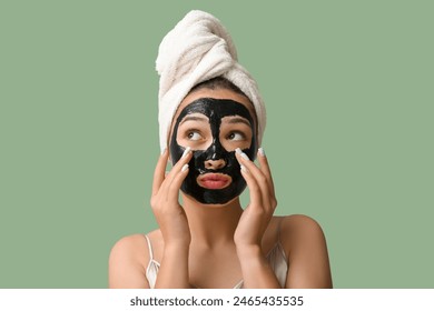 Young woman with activated charcoal mask on her face against green background - Powered by Shutterstock