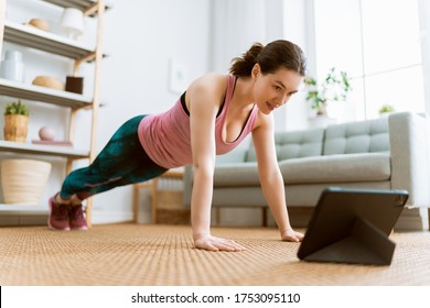 Young woman in activewear watching online courses on tablet while exercising at home. - Shutterstock ID 1753095110