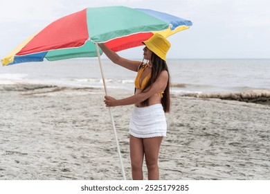 Young woman adjusting a colorful beach umbrella on a sandy shore. - Powered by Shutterstock