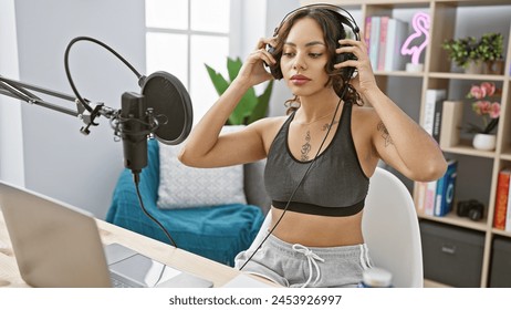 Young woman adjusts headphones in home studio with microphone and laptop - Powered by Shutterstock