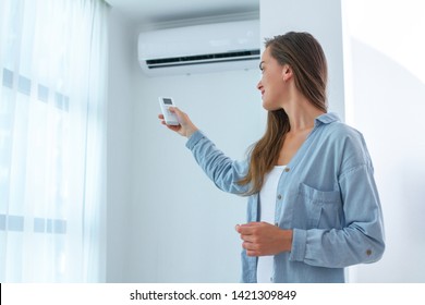 Young woman adjusts the temperature of the air conditioner using the remote control in room at home 