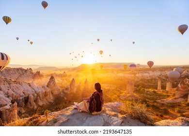 Young woman admire scenery of hot air balloons flying over Love valley with rock formations and fairy chimneys in Cappadocia Turkey - Powered by Shutterstock
