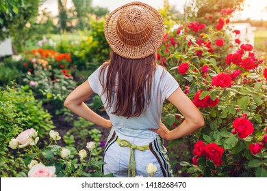 Young woman admiring her summer garden. Gardener in apron and hat looking at flowers. Proud of result. Gardening concept - Powered by Shutterstock