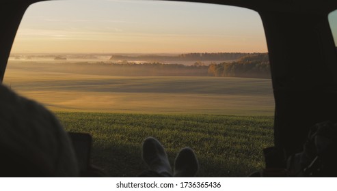 Young Woman Admiring Sunrise In Trunk Of Car Van. Girl Taking Photo On Mobile Phone Against Backdrop Of Nature Panorama In Fog . View From Inside