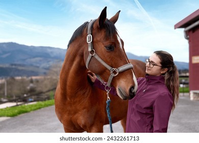 A young woman affectionately interacts with a bay horse, with a picturesque mountainous landscape in the background - Powered by Shutterstock