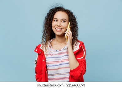 Young Woman Of African American Ethnicity Wear Red Jacket Talk Speak On Mobile Cell Phone Conduct Pleasant Conversation Isolated On Plain Pastel Blue Cyan Background. Wet Fall Weather Season Concept