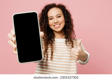 Young woman of African American ethnicity wear light casual clothes hold in hand use close up mobile cell phone with blank screen workspace area show thumb up isolated on plain pastel pink background - Powered by Shutterstock