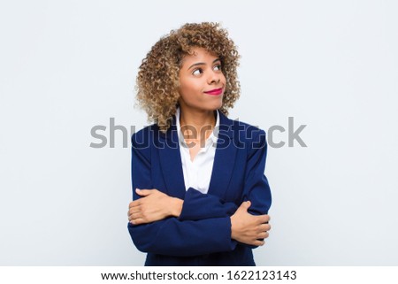 young woman african american shrugging, feeling confused and uncertain, doubting with arms crossed and puzzled look against flat wall