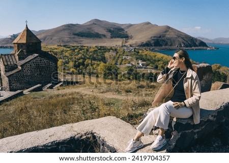 Young woman against Sevanavank monastery, Lake Sevan and mountains on a sunny day in Armenia.