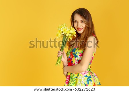 Young woman against yellow wall with flowers in hand in studio