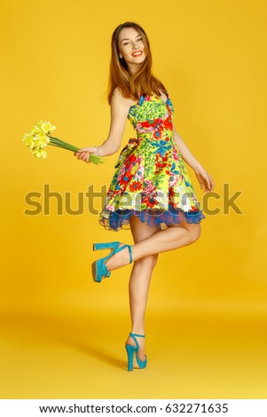 Young woman against yellow wall with flowers in hand in studio