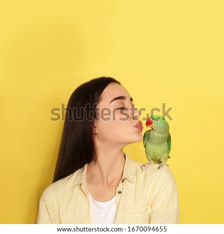 Young woman with Alexandrine parakeet on yellow background, space for text. Cute pet