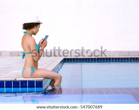 Young woman alone at the pool using mobile phone.