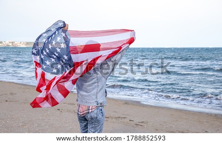 A young woman with an American flag runs by the sea . The concept of patriotism and independence day celebrations.