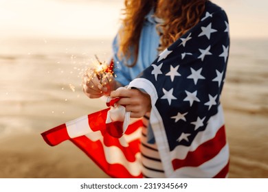 Young woman with American flag  and sparklers on the beach. Patriotic holiday. USA celebrate 4th of July. Independence Day concept - Shutterstock ID 2319345649