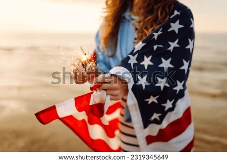 Young woman with American flag  and sparklers on the beach. Patriotic holiday. USA celebrate 4th of July. Independence Day concept