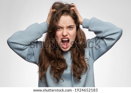 The young woman is angry and screaming, holding her head. Young girl with long hair and blue clothes.